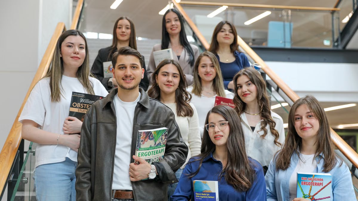 Diverse group of students smiling on stairs, holding educational books indoors.